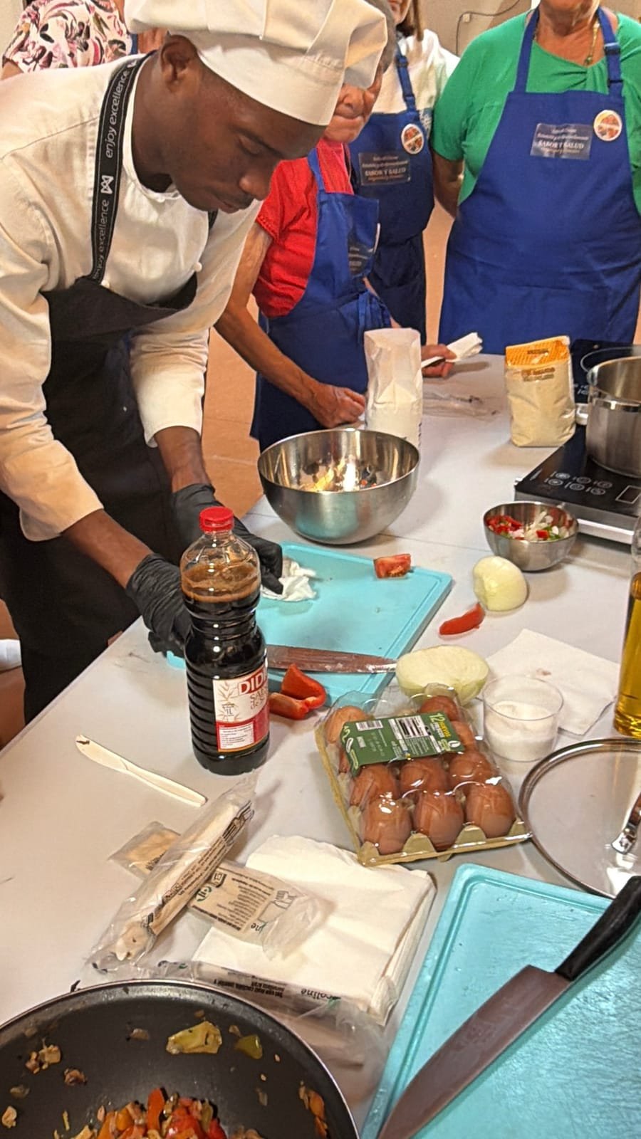Chef y participantes con delantales de Sabor y Salud cocinando durante un taller